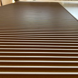 Dehha Szymon Radko - Bliski widok stołu frezarki CNC z widocznymi rowkami i systemem odsysania pyłu w tle.