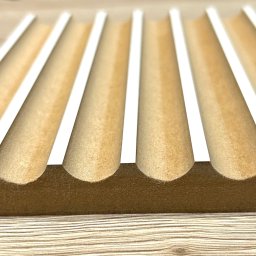 Dehha Szymon Radko - Drewniany element z rowkami, prawdopodobnie forma lub element konstrukcyjny, wycięty z płyty MDF z białymi krawędziami, leżący na drewnianym blacie.