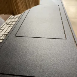 Frezarka CNC w trakcie obróbki grafitowej płyty z wyfrezowanym prostokątnym wgłębieniem. Widoczna głowica frezarki i stół roboczy z rastrem mocującym.