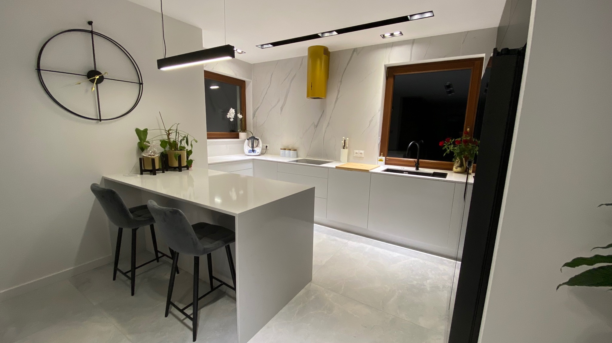 Nowoczesna, jasna kuchnia z wyspą i szarymi hokerami w Szczecinie, z żółtym okapem i marmurowym wykończeniem ściany.