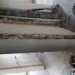 Przygotowanie ściany do wykończenia: zerwana stara okładzina, widoczne ślady po kleju, częściowo zamontowana płyta gipsowo-kartonowa, narzędzia i wiadro z resztkami materiałów na podłodze.