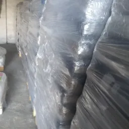 Rząd palet z workami opału owiniętymi przezroczystą folią stretch w magazynie, widoczne fragmenty podłogi i ściany.