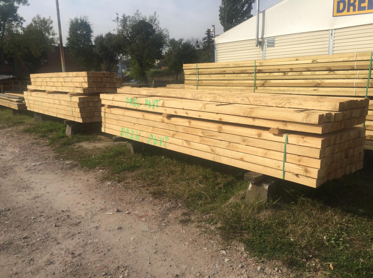 Stosy świeżo przetartego drewna budowlanego, zabezpieczone zieloną taśmą, ułożone na betonowych podstawach na placu składowym.