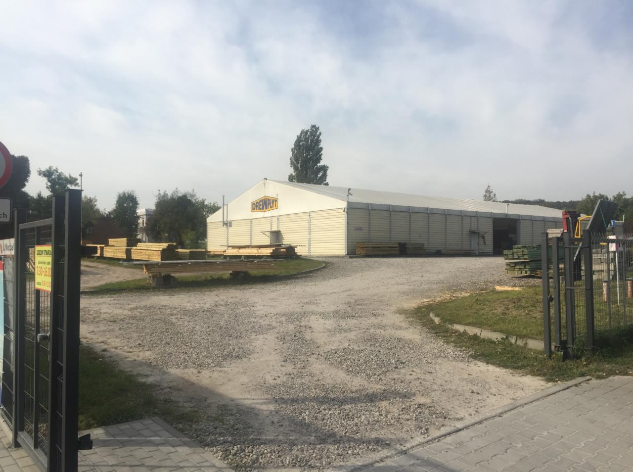 Siedziba firmy Drewpłyt z zapasem drewna na zewnątrz, widok na magazyn z logo firmy i ułożone deski.