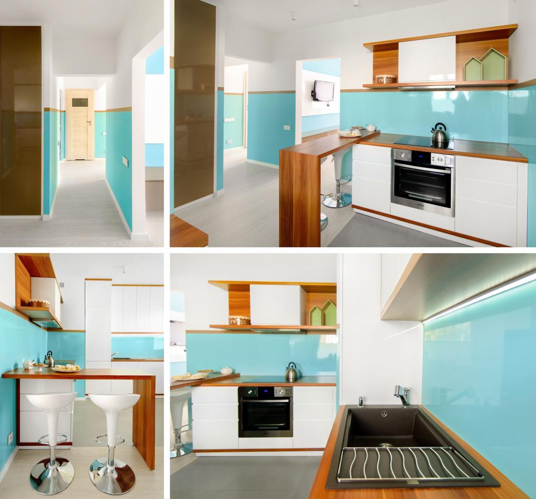 Wnętrze nowoczesnej kuchni z turkusowymi panelami ściennymi, białymi szafkami i drewnianymi blatami, widok na korytarz z brązową szafą w zabudowie.