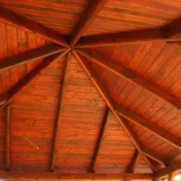 Wnętrze drewnianej altany z widoczną konstrukcją dachu, pomalowaną na ciemny, ciepły odcień brązu, z regularnym układem desek i belek.