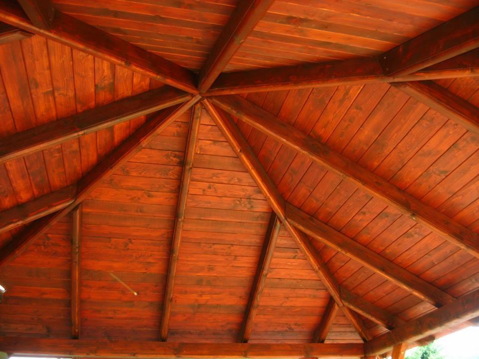 Wnętrze drewnianej altany z widoczną konstrukcją dachu, pomalowaną na ciemny, ciepły odcień brązu, z regularnym układem desek i belek.