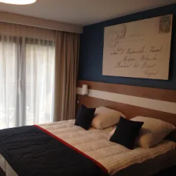 Pokój hotelowy z łóżkiem małżeńskim, drewnianym wezgłowiem i plakatem stylizowanym na pocztówkę na niebieskiej ścianie.