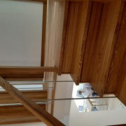 Stolarstwo Marek Wiśniewski - Widok z góry na drewniane schody z metalowymi poręczami, widoczna osoba na dole schodów, jasne wnętrze.