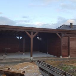 Stolarstwo Marek Wiśniewski - Drewniana wiata garażowa z zamykanym pomieszczeniem gospodarczym w trakcie budowy, widoczne elementy konstrukcyjne i betonowa podstawa, w tle dom jednorodzinny.