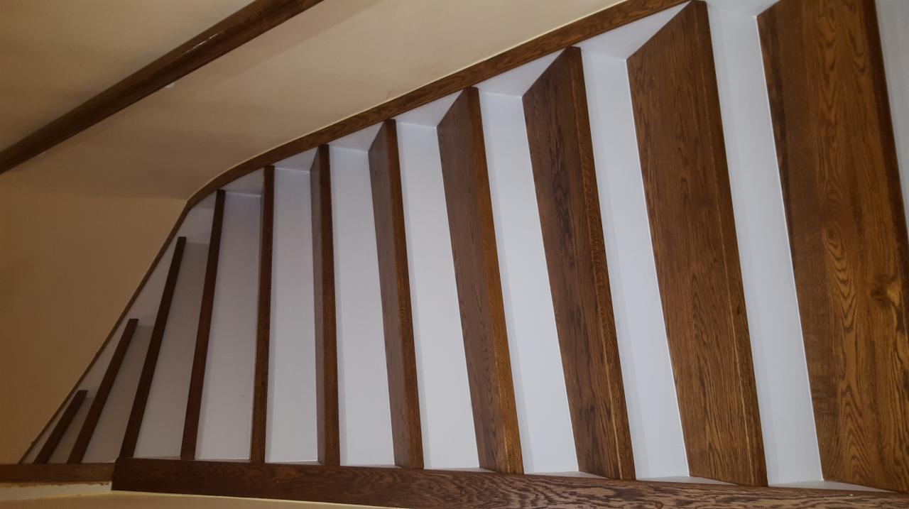 Barierka schodowa z ciemnego drewna z białymi panelami wypełniającymi, widok z dołu, ukazujący zakrzywiony kształt konstrukcji.