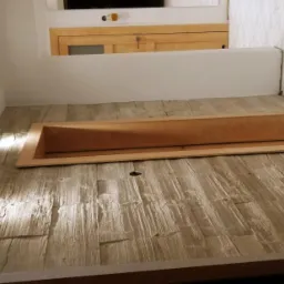 Wykończone wnętrze z podłogą imitującą drewno, oświetleniem punktowym w ścianie i ramą z drewna na podłodze, prawdopodobnie przygotowaną do montażu. W tle widoczna ściana wyłożona płytkami...