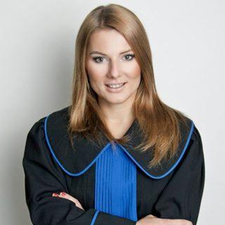 Portret kobiety w todze prawniczej, z rękami skrzyżowanymi na piersiach, na jasnym tle.