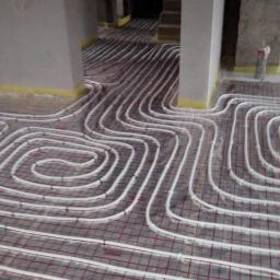 Pio-hydrop - Białe rurki ogrzewania podłogowego ułożone na siatce, widok z góry, surowy stan wykończenia wnętrza, żółta taśma na ścianach.