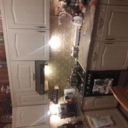 Jasna kuchnia z beżowymi szafkami, ceramiczną płytą grzewczą z garnkami, okapem i wzorzystymi płytkami na ścianie, widziana z perspektywy użytkownika.