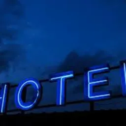 Nocny widok na neonowy szyld 'HOTEL' świecący intensywnym niebieskim światłem na tle ciemnego, burzowego nieba.