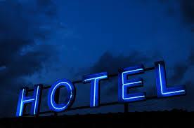 Nocny widok na neonowy szyld 'HOTEL' świecący intensywnym niebieskim światłem na tle ciemnego, burzowego nieba.