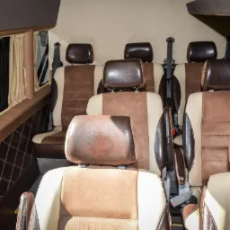Wnętrze luksusowo wykończonego busa z beżowo-brązowymi skórzanymi fotelami, pikowaną tapicerką ścian i zasłonkami w oknach.