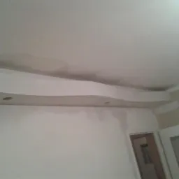 Niedokończone wnętrze z zamontowaną, falistą płytą gipsowo-kartonową na suficie, widoczne ślady szpachlowania i przygotowania do malowania.