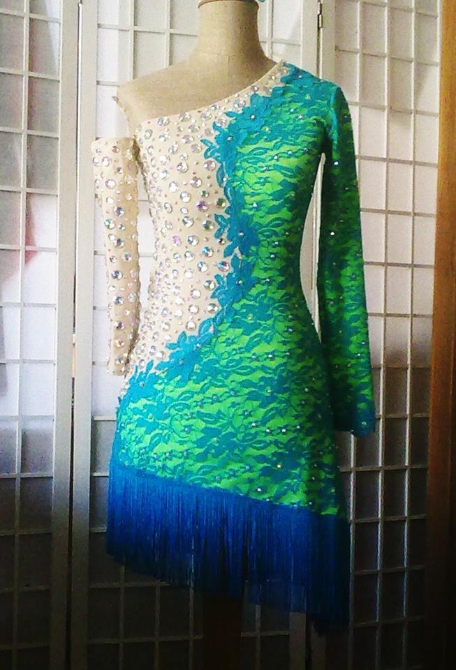 Sukienka taneczna z jednym rękawem, zdobiona koronką w kolorze turkusowym i zielonym, z frędzlami, prezentowana na manekinie.