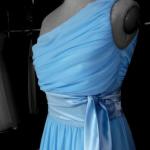 Jasnoniebieska, zwiewna suknia wieczorowa na manekinie, z drapowanym dekoltem na jedno ramię i satynową szarfą w talii.