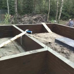 Ruthenia-Group Sp.z o.o - Wykop pod fundamenty domu z izolacją pionową ścian, widoczne wystające pręty zbrojeniowe oraz elementy szalunku, w tle las.