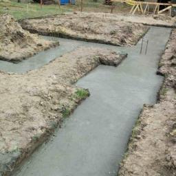 Ruthenia-Group Sp.z o.o - Wylane fundamenty pod dom murowany, widoczne wystające pręty zbrojeniowe, ziemia i przenośna toaleta w tle.