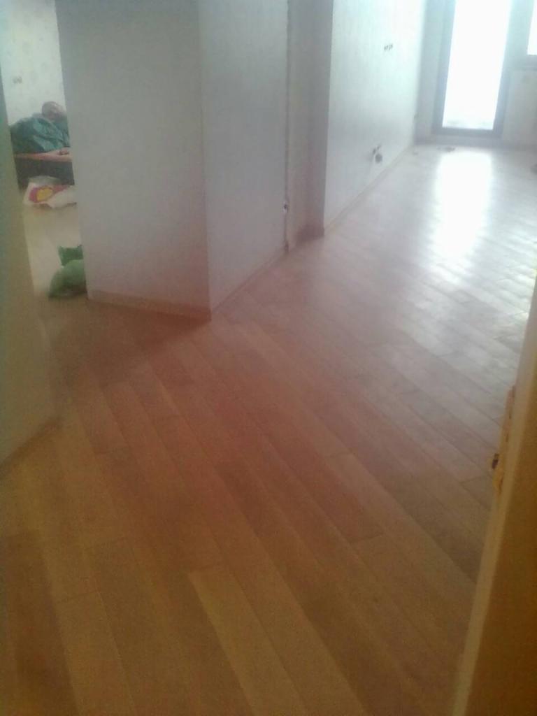 Jasne drewniane panele podłogowe ułożone wzdłuż długiego, pustego korytarza z białymi ścianami w nowym domu.