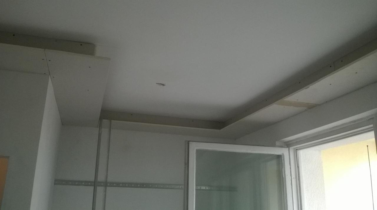 Sufit podwieszany z płyt kartonowo-gipsowych w trakcie montażu, widoczne profile metalowe i łączenia płyt, surowe wykończenie przy oknie.