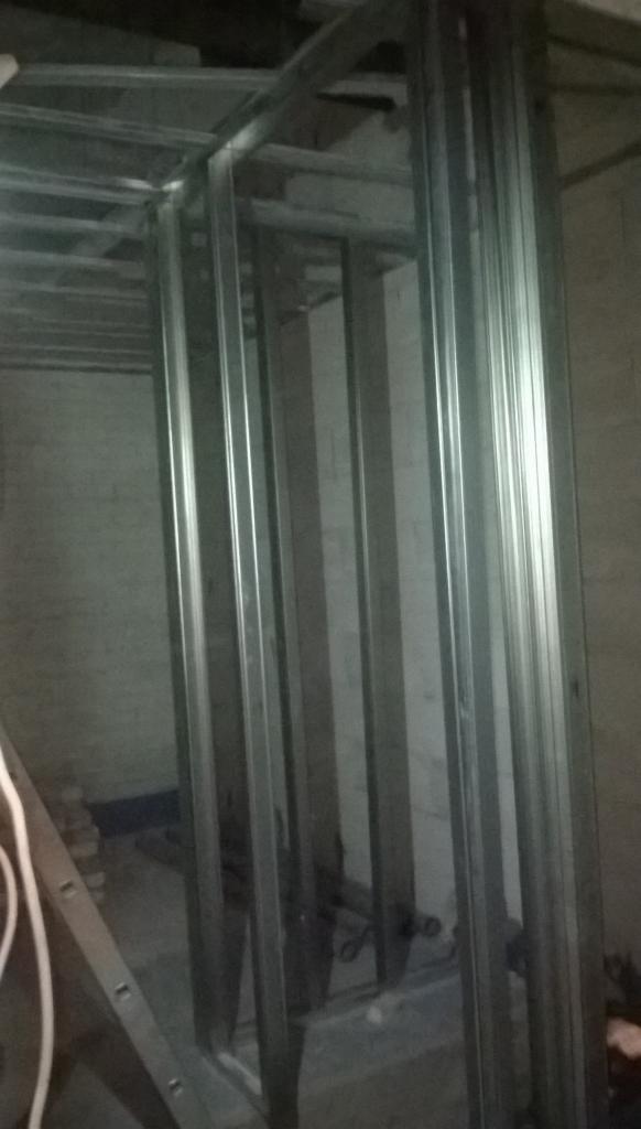 Metalowa konstrukcja szkieletowa ścian działowych w trakcie montażu, widoczne profile pionowe i poziome, surowy stan, ściany w tle częściowo otynkowane.
