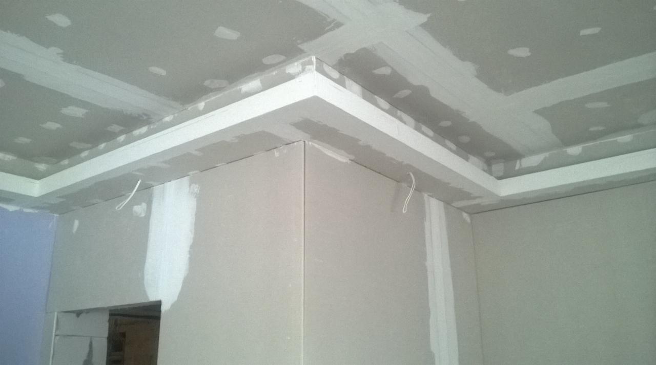 Narożnik pokoju z zamontowaną płytą kartonowo-gipsową, widoczne łączenia płyt wymagające szpachlowania, sufit z dekoracyjnym obniżeniem z płyt G-K, przewód elektryczny zwisający ze ściany.