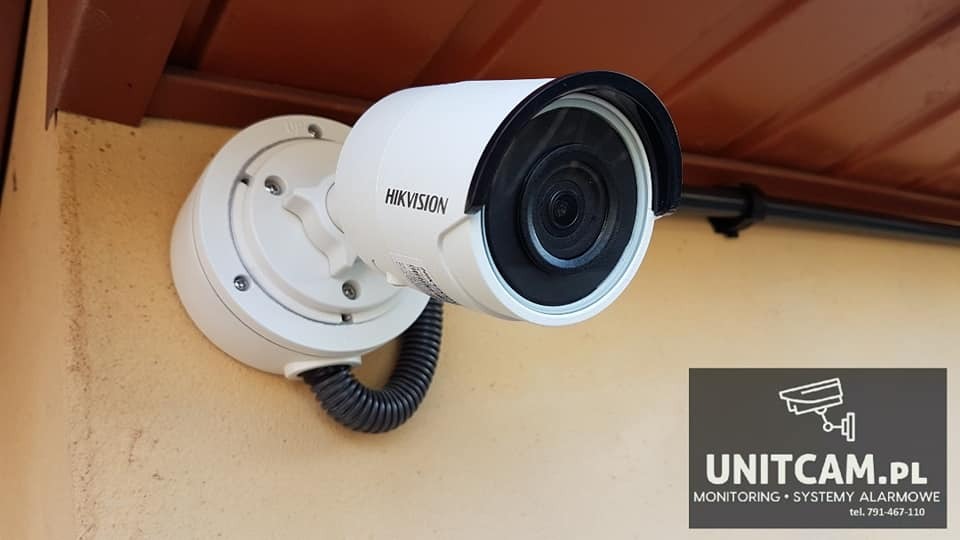 Kamera monitoringu Hikvision zamontowana na elewacji budynku, widoczny peszel kablowy i uchwyt montażowy.