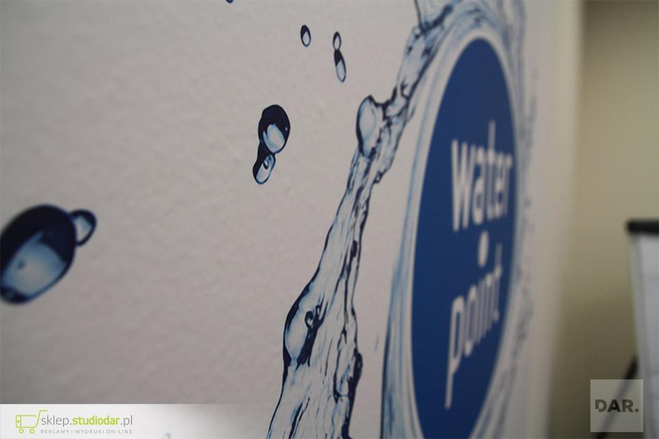Niski kąt ujęcia na folię ścienną z motywem wody i napisem 'Water Point' w niebieskim okręgu.