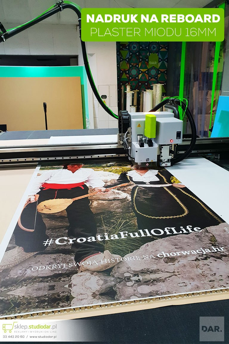 Drukarka wielkoformatowa tnie wydruk na reboardzie o strukturze plastra miodu, przedstawiający parę w strojach ludowych i hasło #CroatiaFullOfLife.