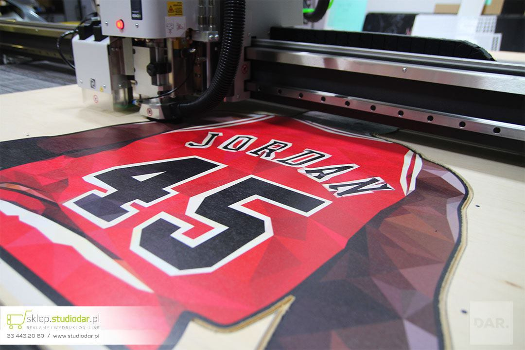 Drukarka wielkoformatowa frezuje sklejkę z nadrukowanym wzorem koszulki sportowej z napisem JORDAN i numerem 45.