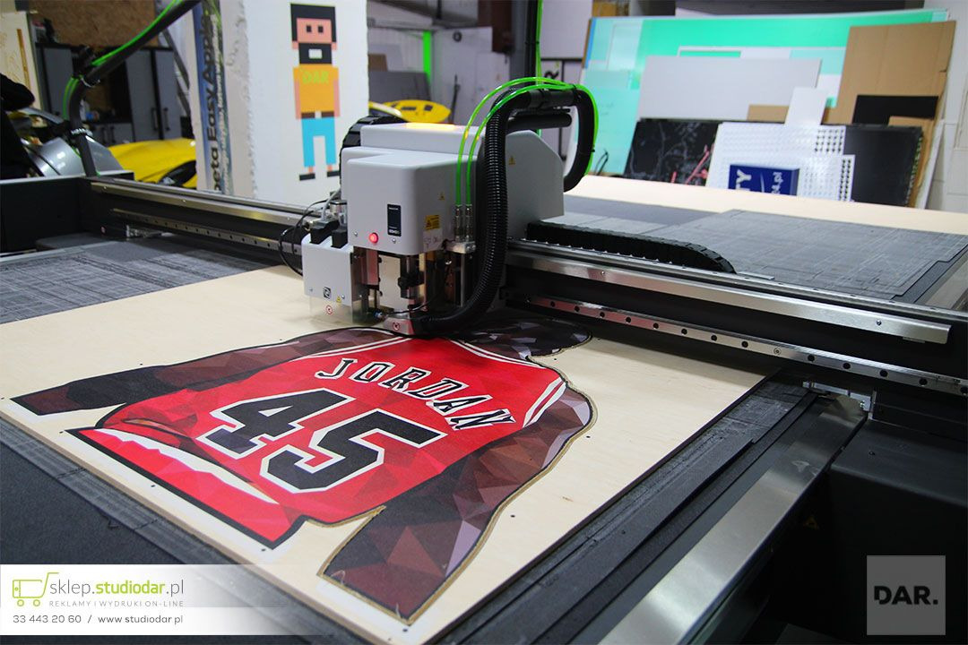 Drukarka frezująca w Bielsko-Białej wycina z zadrukowanej sklejki kształt koszulki sportowej z nazwiskiem Jordan i numerem 45.