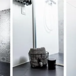 Nowoczesna łazienka z czarną armaturą, heksagonalną podłogą i wzorzystymi płytkami pod prysznicem, uzupełniona o białą umywalkę z szafką i dekoracyjny grzejnik.