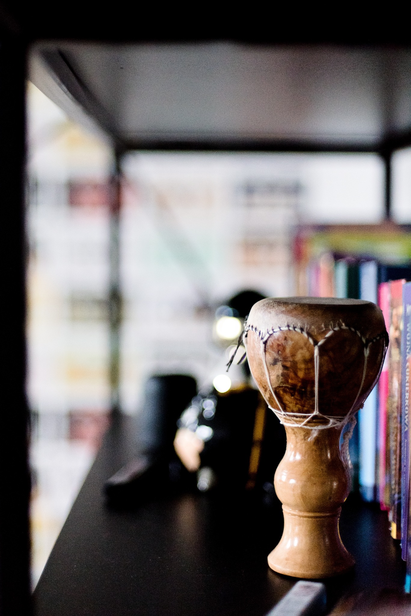 Mały, etniczny bębenek na półce z książkami, oświetlony naturalnym światłem, stanowiący element dekoracyjny wnętrza.