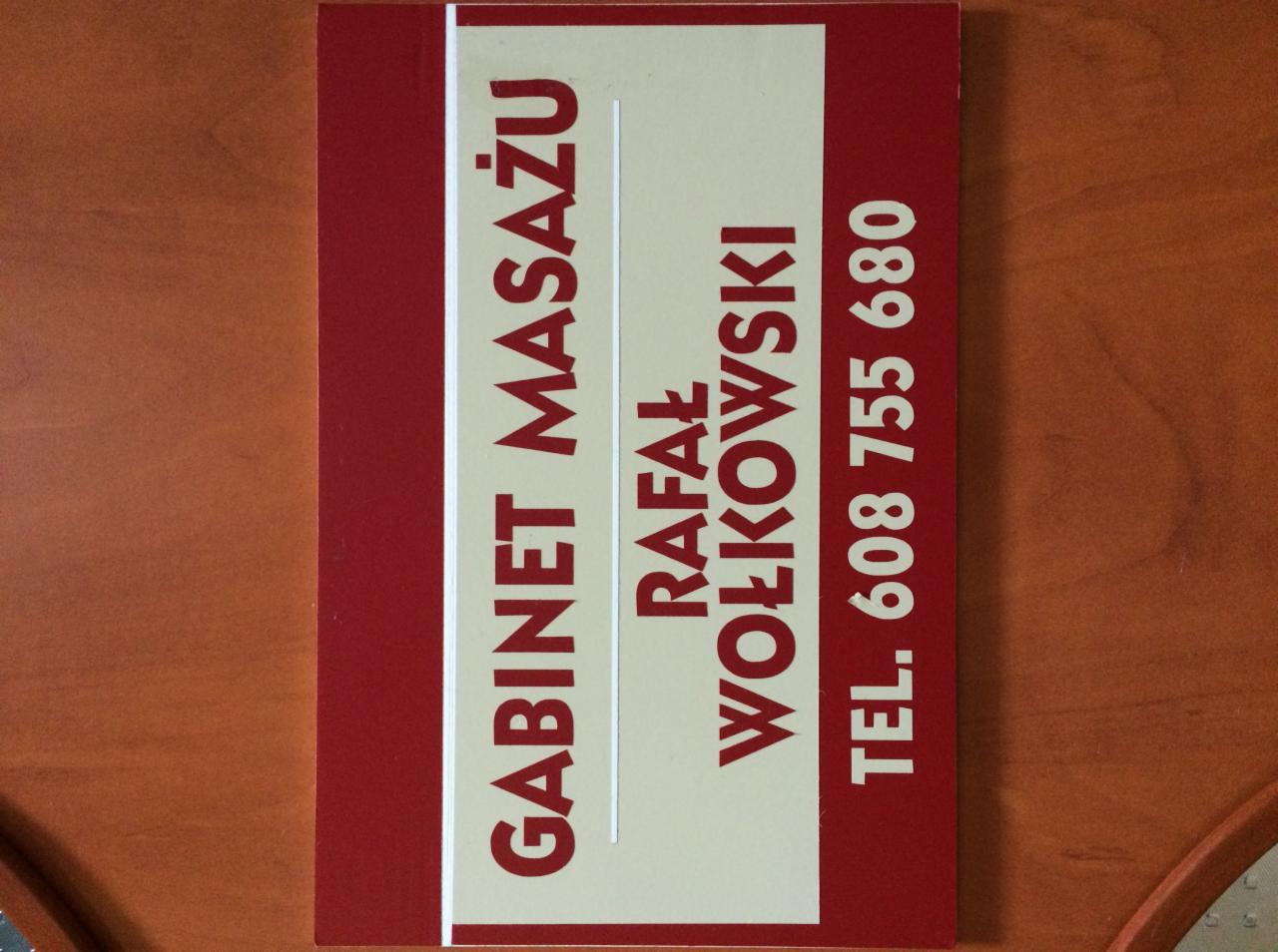 Wizytówka gabinetu z napisem 'Gabinet Masażu Rafał Wołkowski' i numerem telefonu na tle drewnianego blatu.