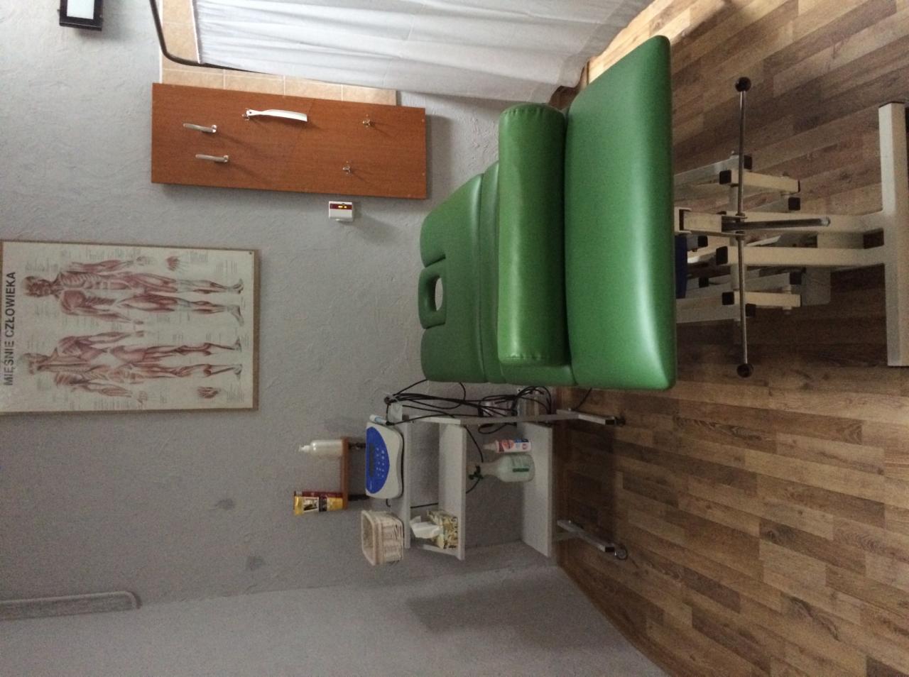 Zielony stół do masażu z regulowanym zagłówkiem, widoczny plakat z układem mięśni człowieka na ścianie, drewniana podłoga