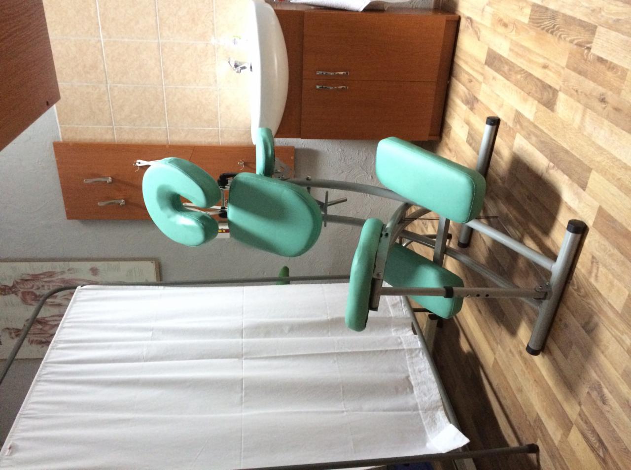 Turkusowy, regulowany stół do terapii manualnej z wycięciem na twarz i zagłówkiem, przykryty białym prześcieradłem w gabinecie z drewnianą boazerią.