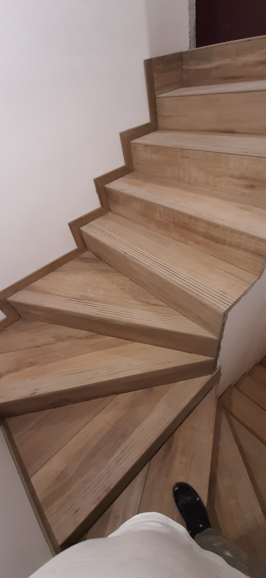 Schody wykończone płytkami imitującymi drewno, widok z góry, częściowo widoczna noga w czarnym bucie.
