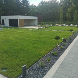 Ogrodowe Sprawy S.C. Przemysław Kubiak Katarzyna Kubiak - Nowoczesny ogród z równo skoszoną trawą, ścieżką z kamieni i minimalistycznym budynkiem w tle. Oświetlenie ogrodowe w postaci kul.