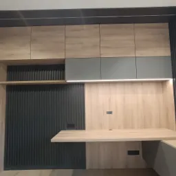 Nowoczesna zabudowa kuchenna z drewnianymi szafkami, szarymi akcentami i podświetleniem LED, uzupełniona o panel ścienny w geometryczny wzór.