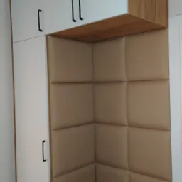 Biała szafa z drewnianymi akcentami i siedziskiem z tapicerowanymi panelami wnękowymi, tworząca minimalistyczną przestrzeń do przechowywania i odpoczynku.