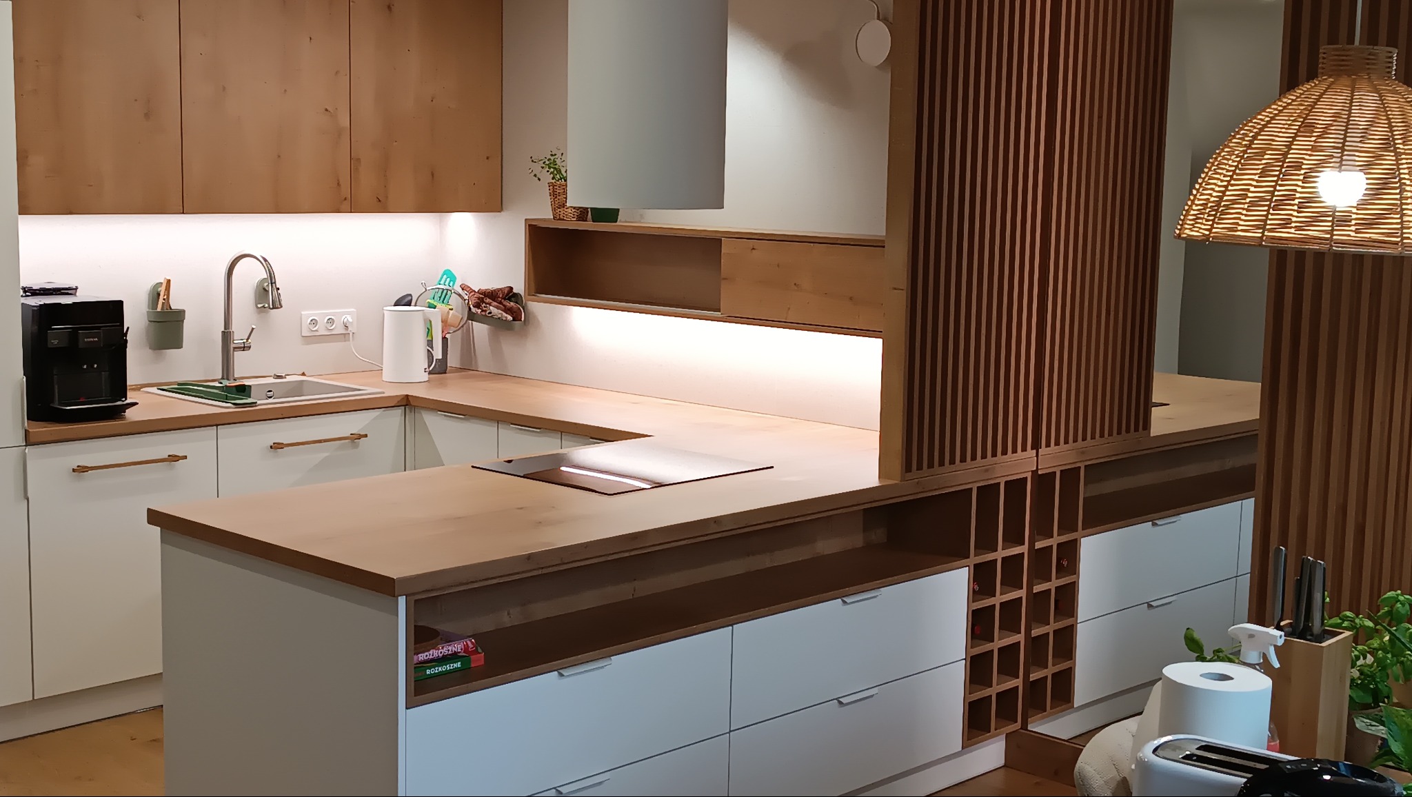 Nowoczesna kuchnia z drewnianymi akcentami: szafki górne, blat i dekoracyjna ścianka z pionowych listew. Wyspa kuchenna z płytą indukcyjną i miejscem na wino.