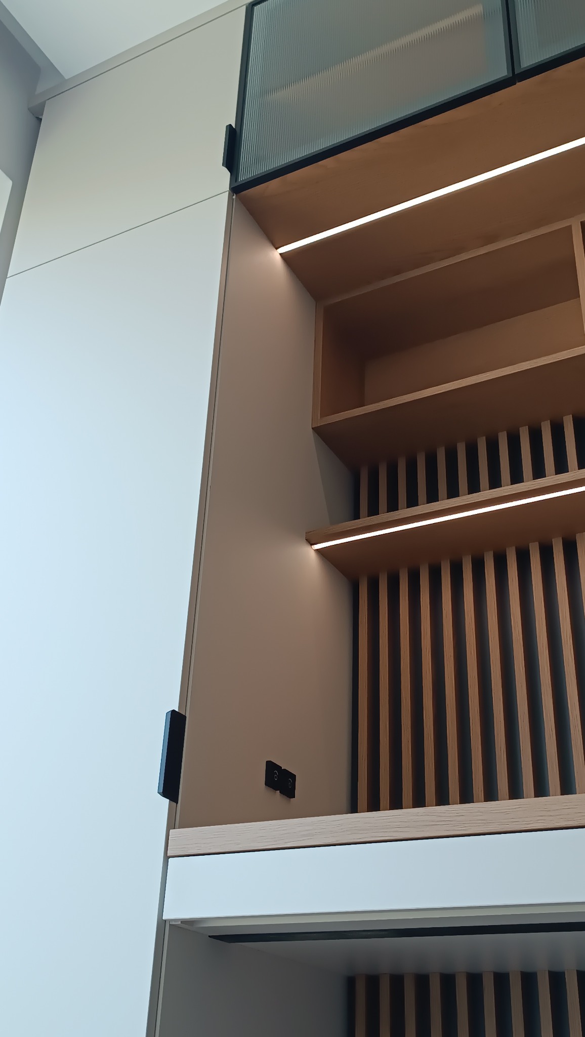 Nowoczesna zabudowa kuchenna z oświetleniem LED, drewnianymi lamelami i ryflowanym szkłem, widziana z dołu pod kątem. Minimalistyczny design.