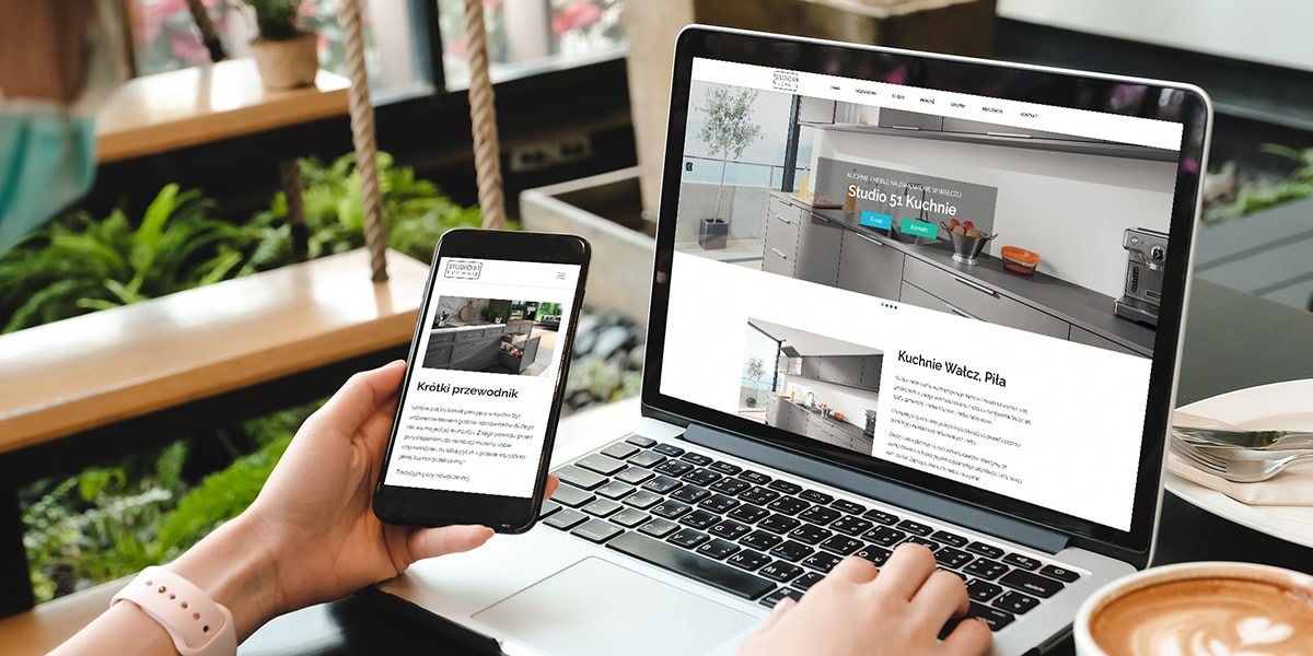 Osoba przegląda na laptopie i smartfonie stronę internetową Studio 51 Kuchnie, prezentującą aranżacje kuchni w szarych odcieniach.