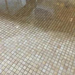 Mokra, wyczyszczona powierzchnia z drobnej, kwadratowej kostki brukowej w odcieniach beżu i brązu, z widocznymi refleksami świetlnymi.