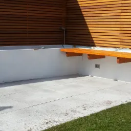 Nowoczesny taras w Tarnowie z drewnianą zabudową i siedziskiem, wykończony jasną kostką brukową i fragmentem trawnika.